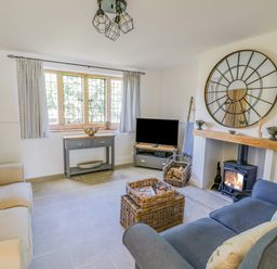 A living room with a sofa a television a fireplace with fire and a round mirror above at Blossom Cottage in Broadway
