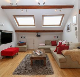 A living room with a beige sofa with red cushions a wooden coffee table on a rug and skylights at Apartment 2 Gorwel Glas in Llanbedrog