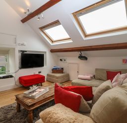 A living room with a beige sectional sofa red cushions wooden coffee table mounted TV and skylight windows at Apartment 2 Gorwel Glas in Llanbedrog