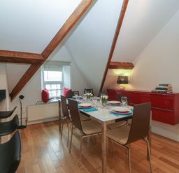 A dining area with a set table and six chairs under a slanted ceiling with exposed wooden beams at Apartment 2 Gorwel Glas in Llanbedrog