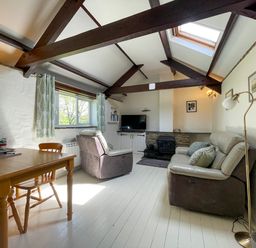 A living room with wood beams a table two chairs two armchairs a television and a fireplace at The Stable @ Canllefaes Penparc near Cardigan