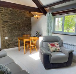 A living room with a gray armchair and wooden table near a stone wall and window at The Stable @ Canllefaes in Penparc near Cardigan