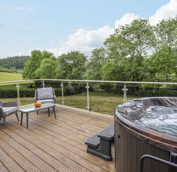 An outdoor deck with two chairs a table and a hot tub overlooking trees and fields at The Cabin at Evelyns Retreat in Glyndyfrdwy