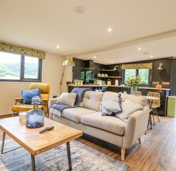 A living room with a sofa, armchair, coffee table, and an open kitchen with dining area at The Cabin at Evelyns Retreat in Glyndyfrdwy