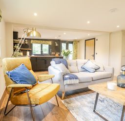 A living area with a yellow armchair and a white sofa with blue cushions a wooden coffee table and kitchen in the background at The Cabin at Evelyns Retreat in Glyndyfrdwy