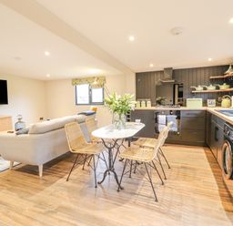 An open living room and kitchen with a sofa a dining table with four chairs and kitchen appliances at The Cabin at Evelyns Retreat in Glyndyfrdwy