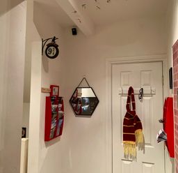 A hallway with a Platform 9 3 4 sign a hexagonal mirror a red and yellow scarf hanging on a door and red brochure holders at The Wizards Loft in Alnwick