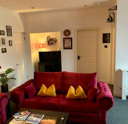 A living room with red sofas yellow cushions framed pictures a table with books and a lamp at The Wizards Loft in Alnwick