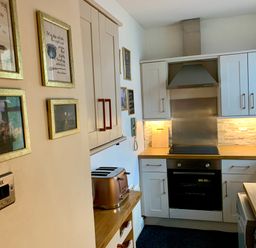 A kitchen with white cabinets wooden countertops a copper toaster and framed pictures on the wall at The Wizards Loft in Alnwick