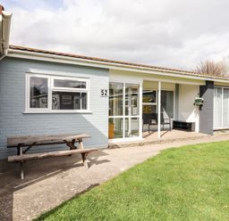 Exterior of a single-story house with a wooden picnic table and green lawn at Marsh Bungalow in Lowestoft