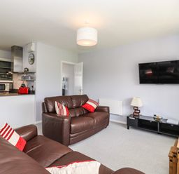 A living room with brown leather sofas pillows a wall-mounted TV a black cabinet and an open kitchen at Marsh Bungalow in Lowestoft