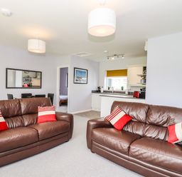 A living room with two brown leather sofas with red and white pillows an open kitchen and a dining area at Marsh Bungalow in Lowestoft