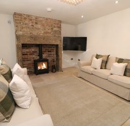 A living room with two beige sofas a stone fireplace with a lit stove and a mounted television at Bramwell House in Corbridge