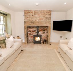 A living room with two sofas facing a brick fireplace with a wood stove and a wall-mounted TV at Bramwell House in Corbridge