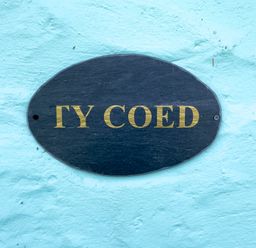 A close up of a black oval sign with gold letters on a light blue textured wall at Ty Coed @ Canllefaes in Penparc near Cardigan