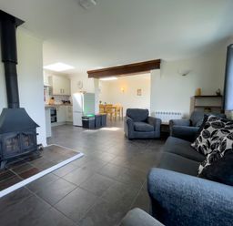 A living room with armchairs a sofa a wood burning stove and a kitchen with a dining table at Ty Coed @ Canllefaes in Penparc near Cardigan
