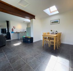A dining area with a wooden table and chairs next to a kitchen with recycling bins and a living area at Ty Coed @ Canllefaes Penparc near Cardigan