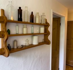 A wooden wall shelf with glass and ceramic bottles in a hallway with wooden doors at The Granary @ Canllefaes in Penparc near Cardigan
