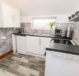 A kitchen with white cabinets a small refrigerator a microwave oven a kettle and a window with flowers on the sill at Hawthorn Dale Cottage Whitby