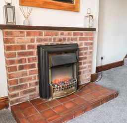 A fireplace with a brick surround and red tile hearth in a room with gray carpet at Hawthorn Dale Cottage Whitby