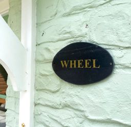 A black oval sign with gold letters saying Wheel on a pale green textured wall at The Wheel @ Canllefaes in Penparc near Cardigan