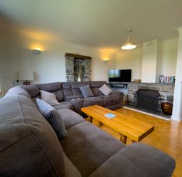 A living room with a large sectional sofa a wooden coffee table a fireplace and a mounted television at The Wheel @ Canllefaes in Penparc near Cardigan