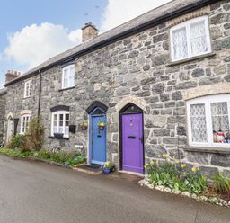 A street view of stone cottages with colorful doors and flowerbeds in front at Coed Y Glyn in Llanuwchllyn near Bala