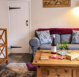 A living room with a gray sofa with animal print cushions and a wooden coffee table with a wine bottle and two glasses at Coed Y Glyn in Llanuwchllyn near Bala