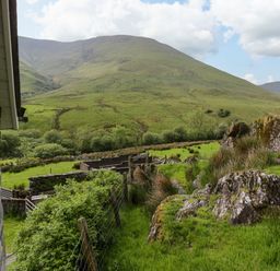 A view of green hills with rocks and a fence beside a stone building at Pennant Tigi Uchaf in Dinas Mawddwy