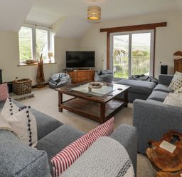 A living room with gray sofas a wood stove a wooden coffee table and a television at Pennant Tigi Uchaf in Dinas Mawddwy