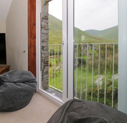 A corner of a room with a television on a wooden stand and bean bags near glass doors overlooking green hills at Pennant Tigi Uchaf in Dinas Mawddwy