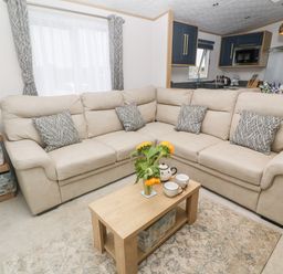 A living room with a beige sectional sofa and patterned cushions at Chantry Lodge in Hendra Croft near Goonhavern