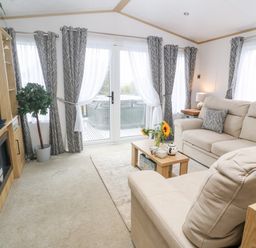 A living room with a beige sofa a television and a coffee table with flowers at Chantry Lodge in Hendra Croft near Goonhavern