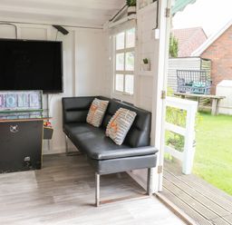 A room with a black sofa and two pillows a large television on the wall a sign that reads home and a door opening to a garden at Wyvill House in Cayton