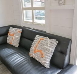 A black leather sofa with two decorative cushions near a window and an open door showing a grassy area at Wyvill House in Cayton