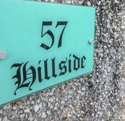A green house number sign 57 Hillside mounted on a pebble textured wall at Hillside in Gunnislake