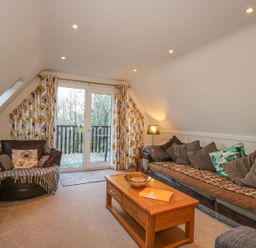 A living room with a sofa armchair coffee table TV and balcony doors at Hillside in Gunnislake