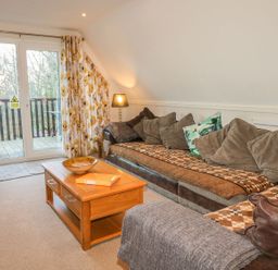A living room with a brown sofa and cushions a wooden coffee table and glass doors leading to a balcony at Hillside in Gunnislake