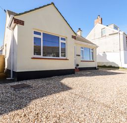 A single story house with large windows and a gravel driveway at Seawynds in Crantock