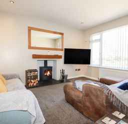 A living room with two sofas a fireplace a wall-mounted television and large windows at Seawynds in Crantock
