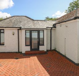 A rear exterior view of a single-story house with a tiled roof and black framed glass door opening onto a red brick patio at Pinewood in Saundersfoot