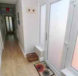 A hallway with wooden flooring a basket a mat and frosted glass door at Pinewood in Saundersfoot
