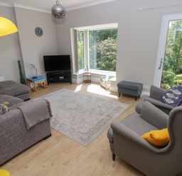 A living room with gray sofas a television and a large window at Pinewood in Saundersfoot