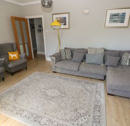 A living room with a gray sofa and armchairs a beige patterned rug a yellow floor lamp and framed pictures on the wall at Pinewood in Saundersfoot