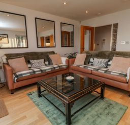 A living room with two brown sofas and a black coffee table on a green rug at A Stone's Throw in Downderry