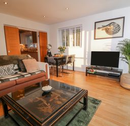 A living room with a sofa a coffee table a TV on a stand a dining table with chairs and a plant at A Stone's Throw in Downderry