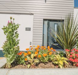 A front entrance with a door and a flower bed with orange and red flowers at Fisherman's Rest in Wyke Regis
