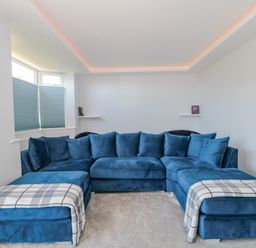 A living room with a blue sectional sofa and two plaid throws near a window with blinds at Fisherman's Rest in Wyke Regis