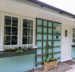 Front entrance of a house with two windows and planters under them and a white door at Honeysuckle Cottage in Crossgates