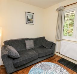 A living room with a grey sofa three cushions a floor lamp round rug and a window at Honeysuckle Cottage in Crossgates